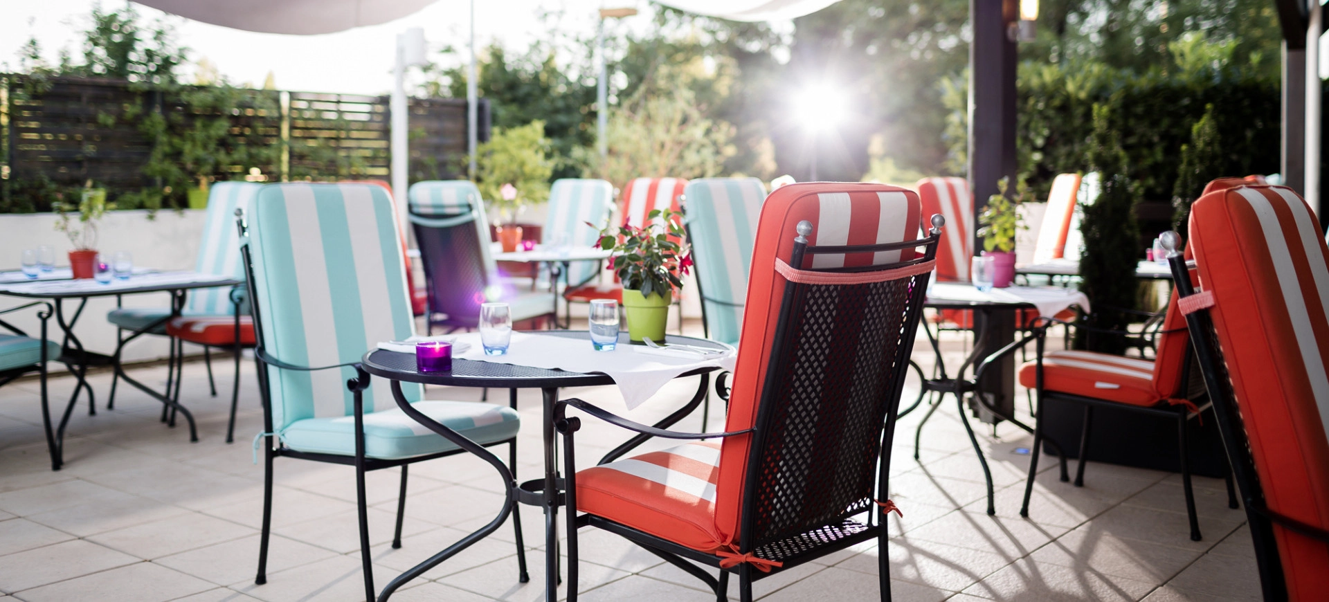 Terrasse ensoleillée d’un restaurant avec des chaises colorées et une ambiance chaleureuse, idéale pour un repas en plein air.