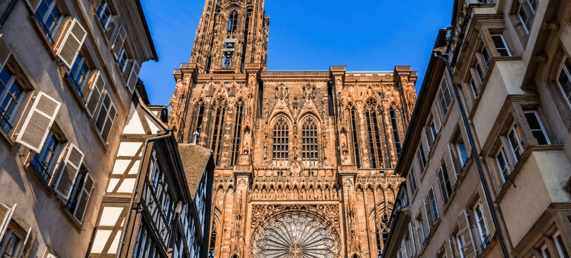Vue impressionnante de la cathédrale de Strasbourg sous un ciel bleu, entourée de bâtiments typiques alsaciens.