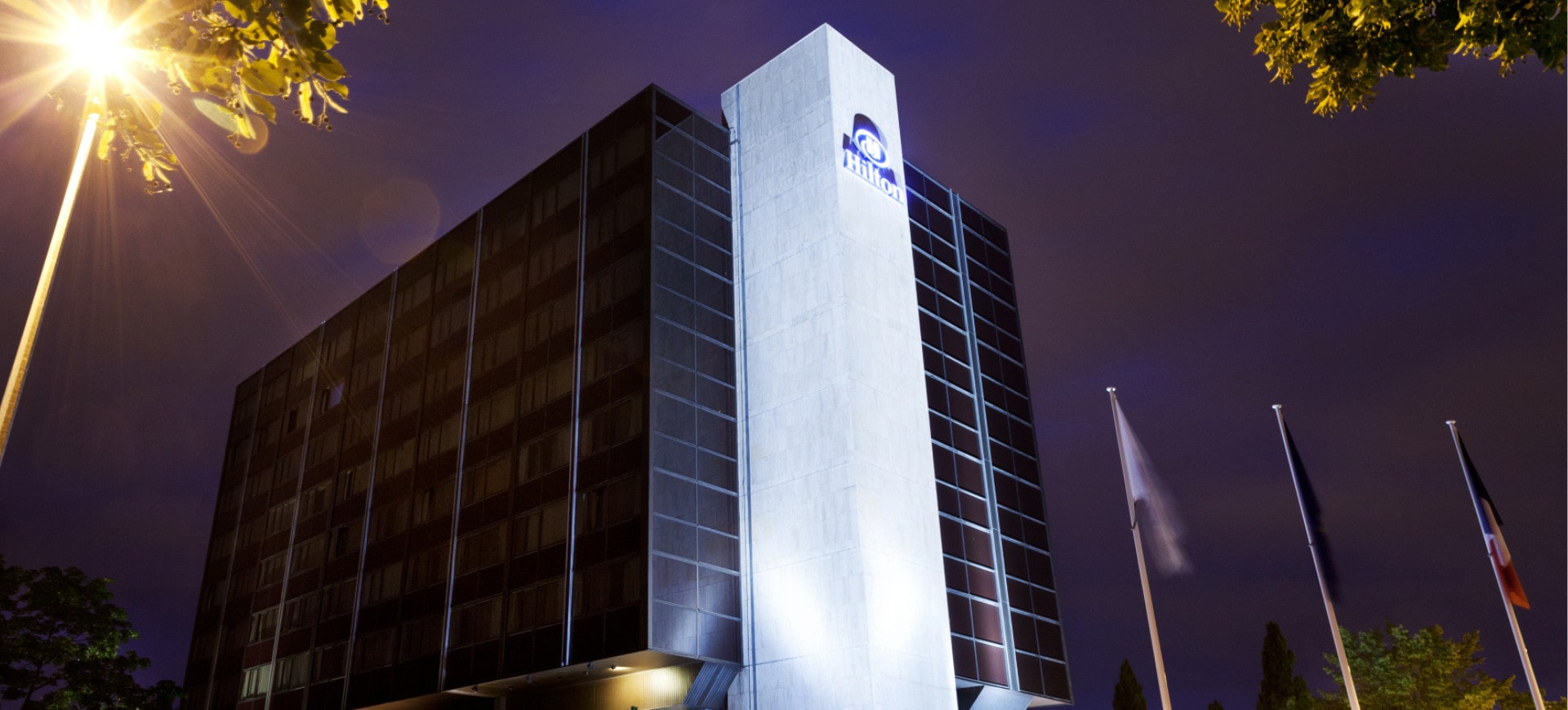 Night view of a modern lit-up hotel, with flags waving at the entrance